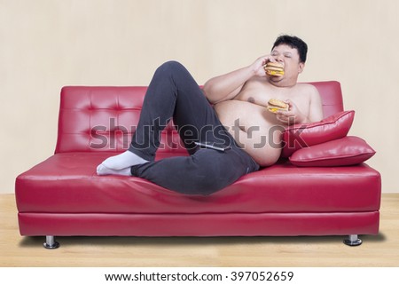 Picture of greedy person feels hungry and eat hamburger while leaning on the couch