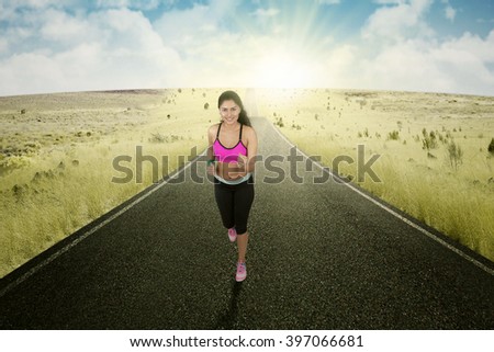 Picture of young female runner doing workout on the road and smiling at the camera, shot in the morning