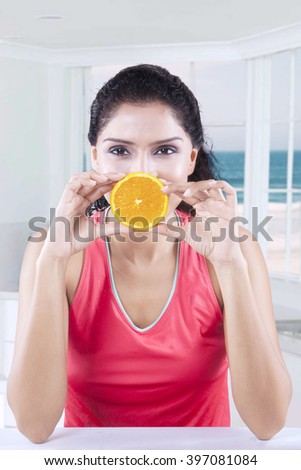 Picture of Indian healthy female model holding an orange slice while sitting in the kitchen
