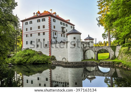 Fairy castle with defense towers, walls and bridge, a pond with reflection in water, medieval Sneznik castle, Slovenia.