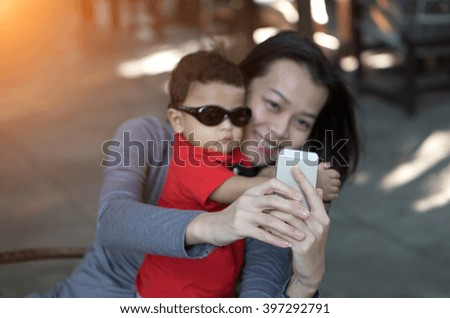 Focus of Asian mother hand and son taking selfie photograph together - Sunlight filter effect