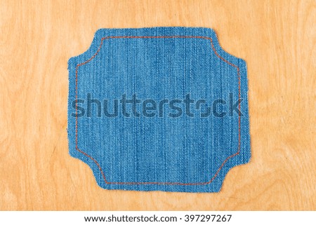 Figured frame made of denim is lying on a light wood surface, with space for text, advertising