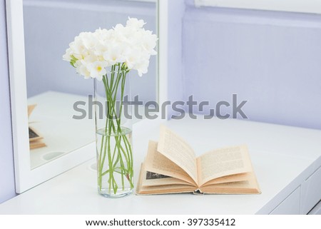Bouquet of white flowers in a vase placed on a table. Cozy picture. Bouquet of white flowers in a vase and a book on a white table.