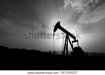 Silhouette of crude oil pump at cloudy sunset in the oil field - Black and white.