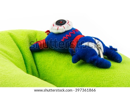 cute furry monster isolated on white background / blue and red children halloween toy / cartoon comic animal / happy birthday gift and present / doll on green fur pillow / hair and velour cloth