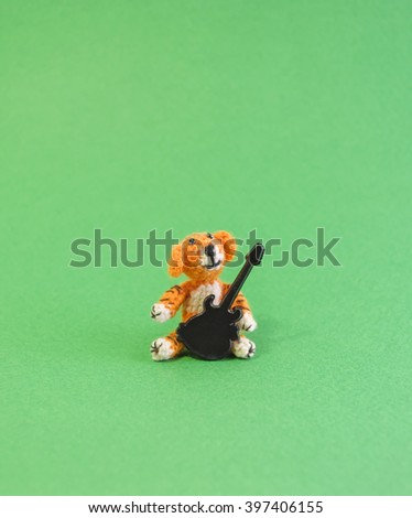 Knitted toy tiger with guitar. Green background.