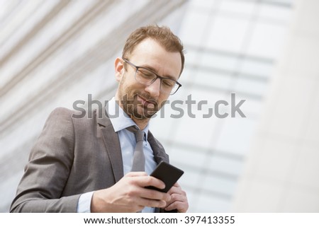 Businessman texting sms in front of the blue glass business building   
