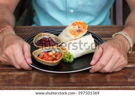 Burrito on ceramic ware, the Man eats a burrito, tasty, it is useful, vegetarian food