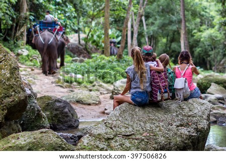 Young tourists are resting on the rocks in the jungle elephants in the background