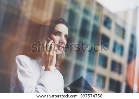 Photo business woman wearing modern white shirt, talking smartphone and holding documents in hands. Open space loft office. Panoramic windows background. Horizontal mockup. Film effect