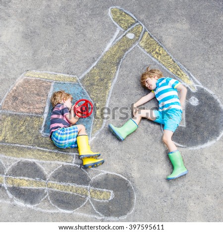Two little happy kid boys having fun with excavator picture drawing with colorful chalk. Creative leisure for children outdoors in summer.