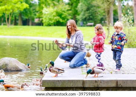 Mother and her children feeding ducks in summer park, adorable kid boy and girl, siblings having fun together Royalty-Free Stock Photo #397598833