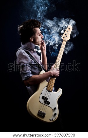 portrait of a man with a guitar and a cigarette on a dark background and a light blue shirt