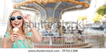 summer, junk food and people concept - young woman or teenage girl in sunglasses eating ice cream over carousel at amusement park background
