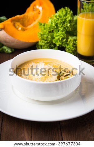 Creamy pumpkin soup with sids and parmesan on dark wooden background close up.