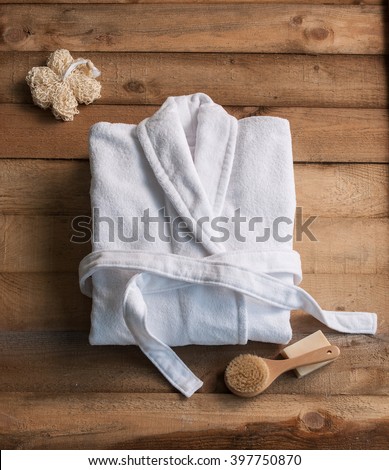 bathrobe bath soap and loofah brush behind wooden table Royalty-Free Stock Photo #397750870