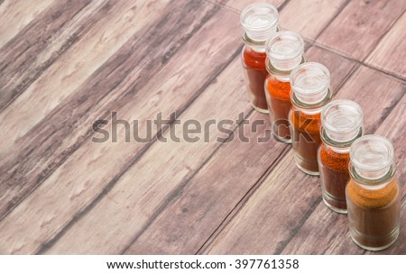 Different type and colors of chilly powder, paprika powder, cayenne powder in glass vial over wooden background