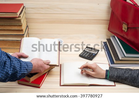 Closeup of business partners hand pointing where to sign a contract, legal papers or application form. On a wooden table books, documents, calculator, red briefcase. Copy space.