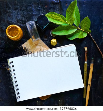 Craft paper background with boho chic style decorations: sketchbook, tree branch, golden paint, ink over black wooden table. Copy space for text. Natural, rustic, ethnic or hipster vintage mock up.