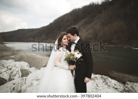Beautifull wedding couple kissing and embracing near river with stones