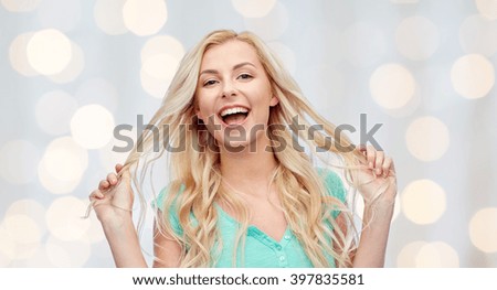emotions, expressions, hairstyle and people concept - smiling young woman or teenage girl holding her strand of hair over holidays lights background