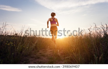 Young sporty girl running on a rural road at sunset in summer field. Lifestyle sports background   Royalty-Free Stock Photo #398069407