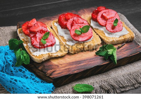 Three sweet fruit sandwich with strawberry, mint on a cutting board on sackcloth with blue lace on a black wooden background surface