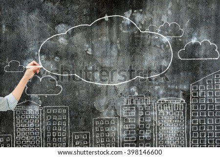 Woman hand holding chalk drawing white clouds and city buildings on dirty concrete wall.