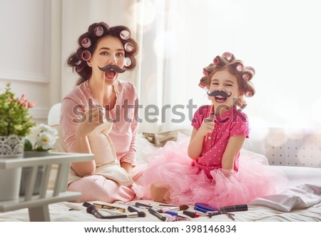 Funny family Mother and her child daughter girl with a paper accessories. Mother and daughter preparing for a party and having fun. Beautiful young woman and funny girl with a paper mustache on stick. Royalty-Free Stock Photo #398146834