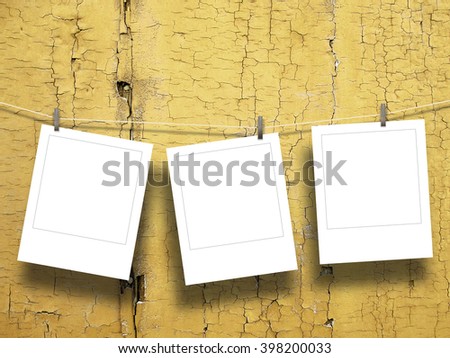 Close-up of three square blank instant photo frames hanged by pegs against yellow wooden boards background