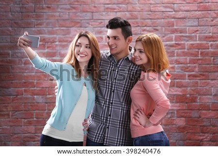 Young people taking selfie with mobile phone on brick wall background