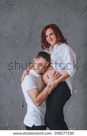 Man is embracing stomach of a pregnant woman. There is a place for Tex. On a gray background. She looks into the camera.