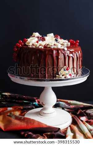 Modern chocolate european cake decorated with flowing glaze and buttercream flowers. Black background. Shallow focus