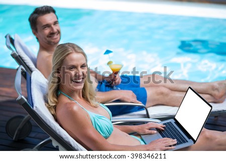Happy couple sitting near pool with a laptop and martini glass