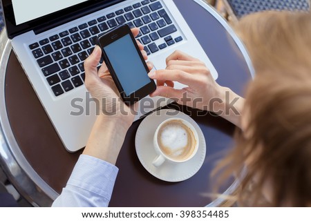 girl holding a mobile phone. Computer and coffee on the table in the cafe. She works outside the home.