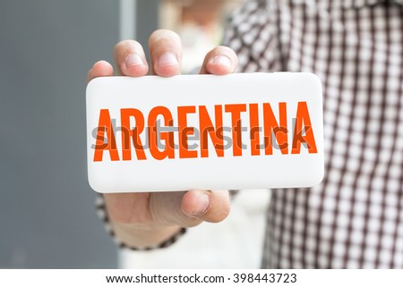 Man hand showing ARGENTINA word phone with  blur business man wearing plaid shirt.