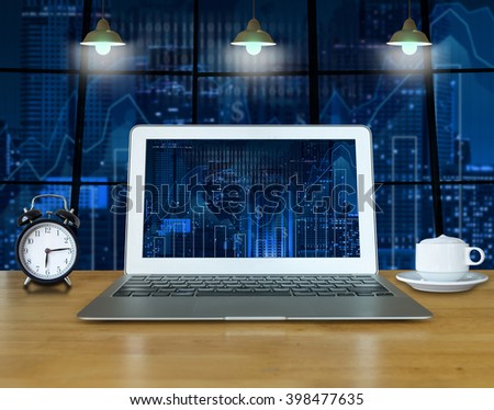 Workspace with computer laptop on the wood table which shown trading graph on the blurred photo of cityscape building background over the screen, trading technology concept