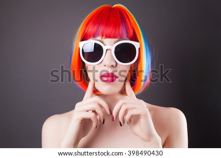 beautiful woman wearing colorful wig and white sunglasses against gray background