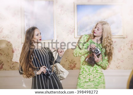 Two female models in fashionable dresses with vintage cameras in vintage interior