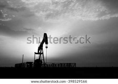 Cloudy sunset and silhouette of crude oil pump in oilfield - black and white