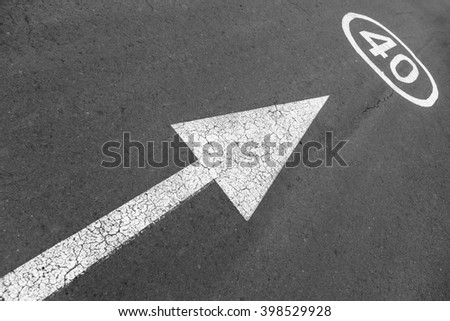 An arrow and street sign on asphalt indicating a maximum speed of 40 kph