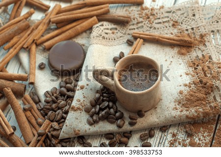 A composition with a handmade earthenware cup of coffee, cinnamon sticks, coffee beans, cocoa powder and a chocolate candy on a cloth surface   