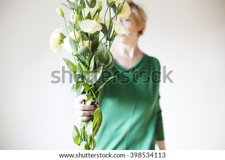 Woman in green shirt holding a large bouquet of white eustoma flowers in hands.
