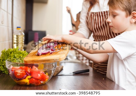 Family cooking background. Small boy help his mother with cutting onion for salad in the kitchen