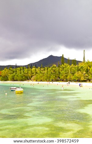 amazing isle of pines ,beach, vacation, holiday, people on the beach , green ,boats ,trees near ,dream island, new caledonia ,wonderful ,cloudy sky ,storm