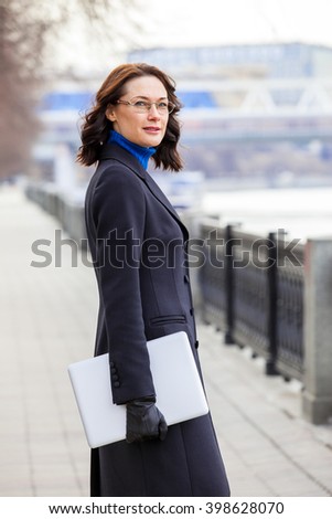 beautiful business middle-aged woman in a dark coat with a laptop outdoors