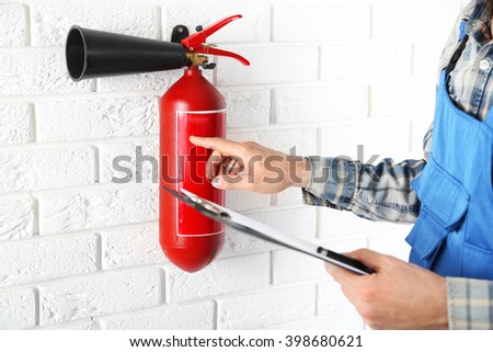 Man inspecting the fire extinguisher against white brick wall background