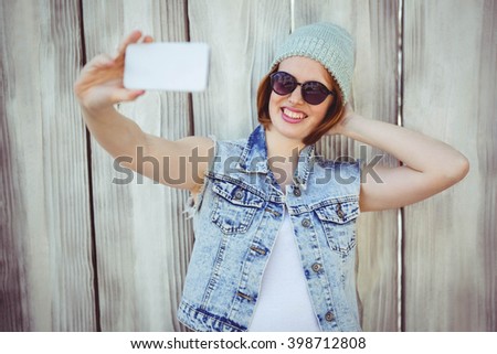 smiling hipster woman taking a selfie against a wooden background
