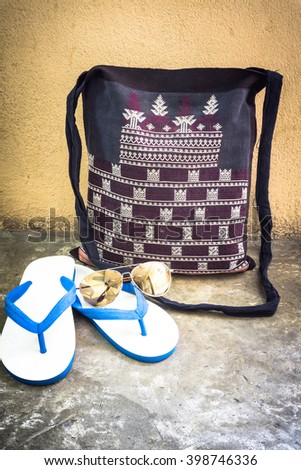 Men's handcrafted bag with slippers and sunglass on cement floor over wall grunge background