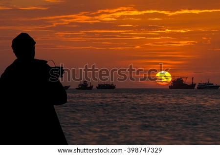 silhouette of photographer taking photo on the Sunset on the sea with colorful sky and fishing boat, Thailand